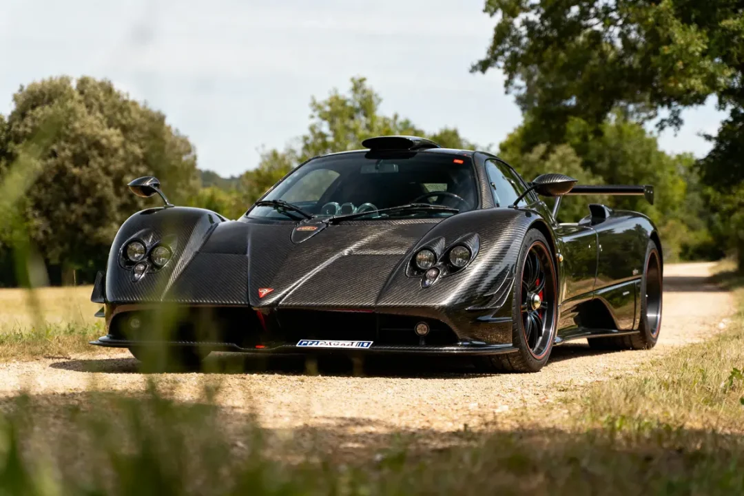 Voiture de sport noire, stationnée sur chemin de terre bordé d'herbe et d'arbres, éclairage naturel.