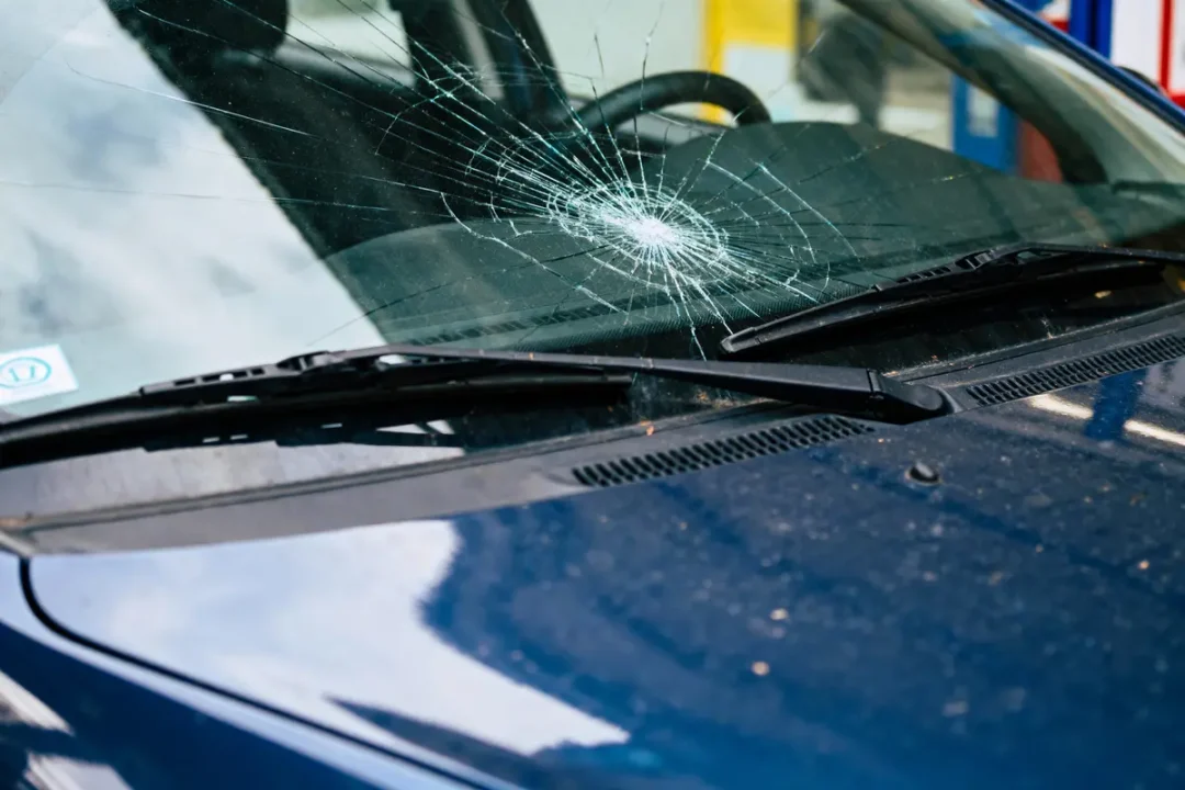 Pare-brise de voiture avec un impact d'éclat circulaire, essuie-glaces visibles, véhicule bleu.