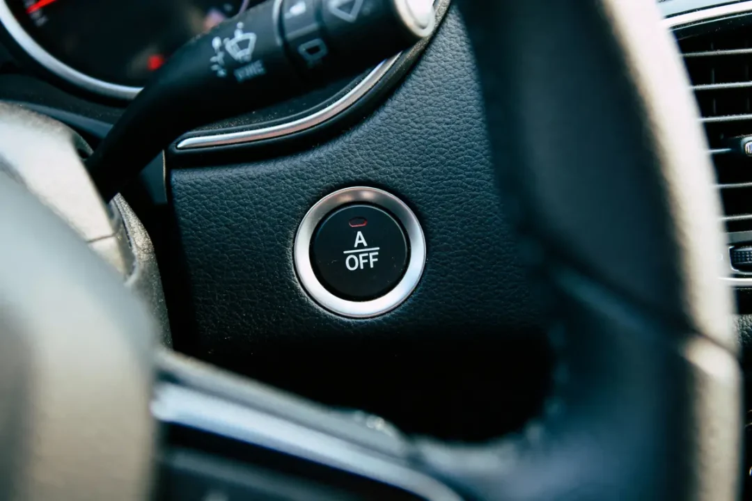 Bouton de désactivation du système Stop-Start dans l'habitacle d'une voiture, entouré de cuir noir.