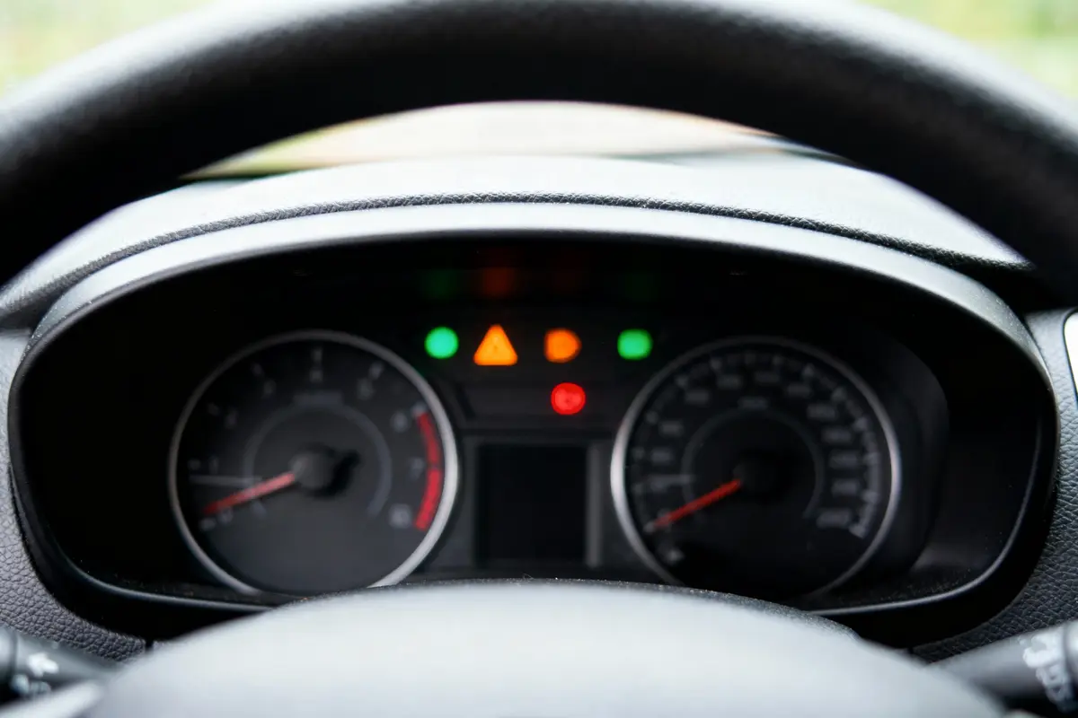 Tableau de bord de voiture avec voyants lumineux allumés, vitesse et compte-tours indiqués, volant visible.