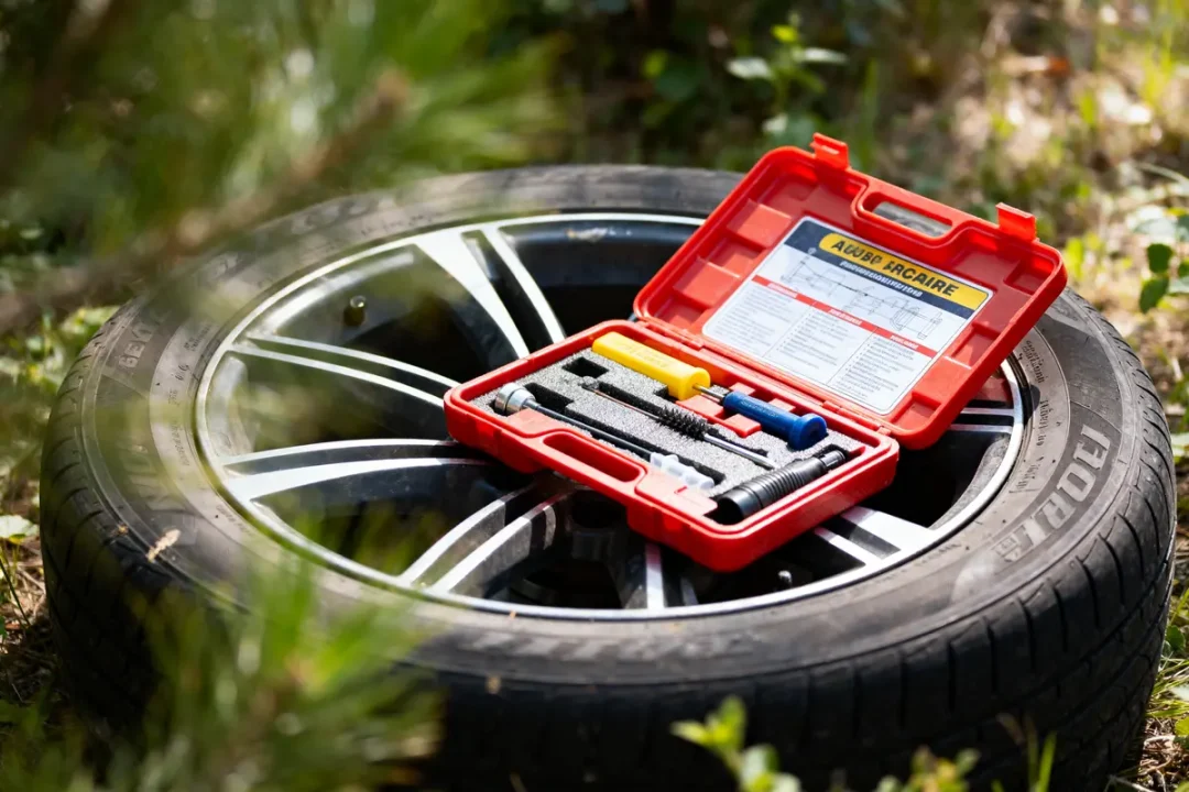 Kit de réparation rouge ouvert sur un pneu de voiture dans un environnement extérieur.