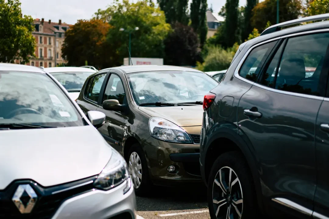 Plusieurs voitures garées dans un parking, entourées d'arbres et de bâtiments en arrière-plan.