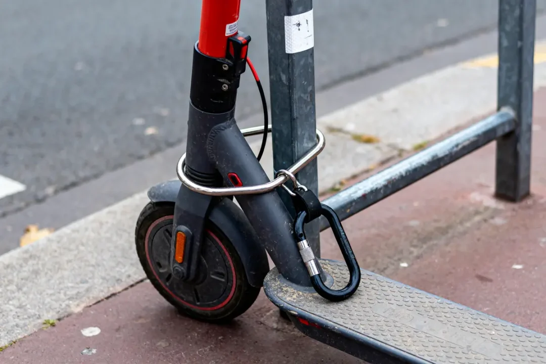 Trottinette électrique sécurisée à un support métallique avec un antivol sur un trottoir urbain.