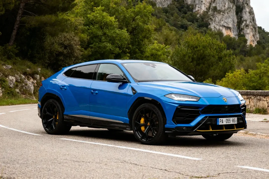 SUV bleu sport sur route sinueuse, entouré de verdure et falaises en arrière-plan. Plaque immatriculation visible.
