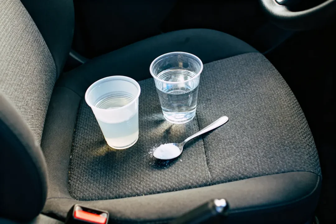 Deux gobelets d'eau et cuillère avec poudre blanche sur siège de voiture.