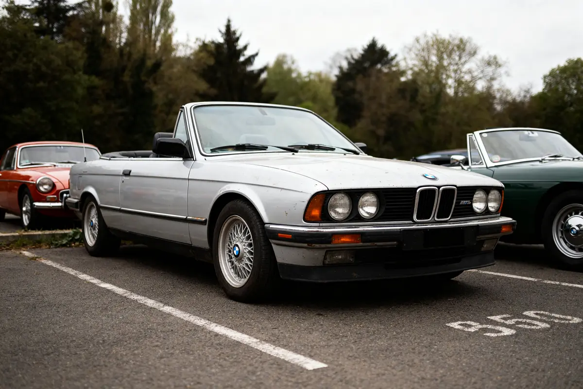 Ancienne BMW décapotable grise garée dans un parking avec d'autres voitures classiques