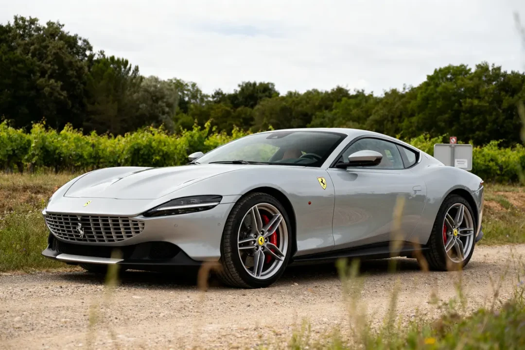 Ferrari Roma grise sur chemin de terre bordé de verdure et de vignes