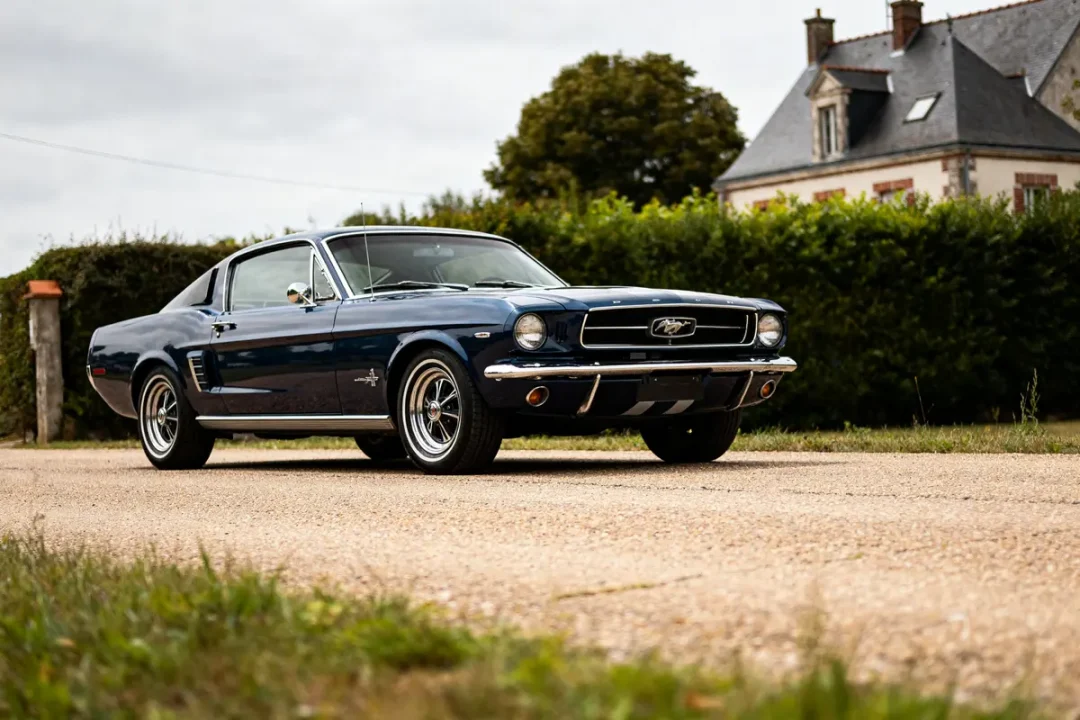Voiture classique Ford Mustang 1967 stationnée devant une maison historique sur route pavée