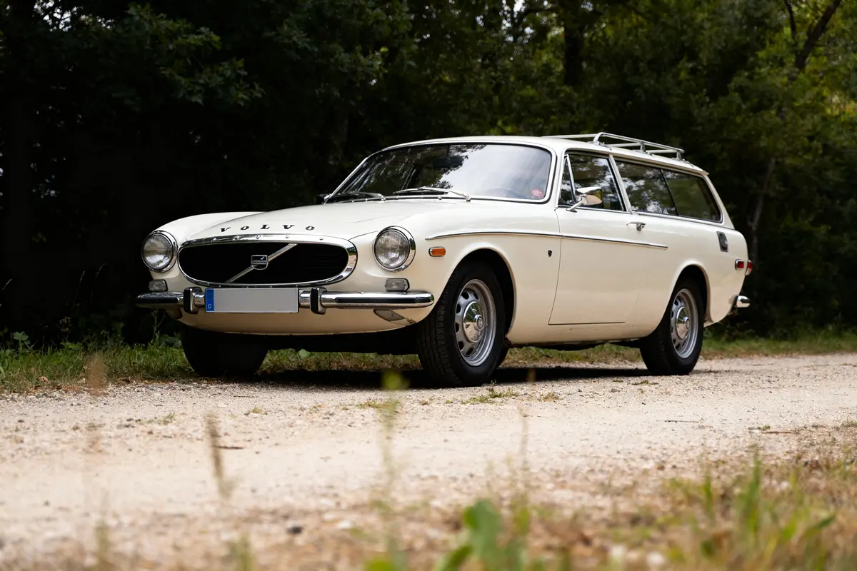 Voiture classique blanche P1800 Volvo wagon stationnée sur une route forestière.
