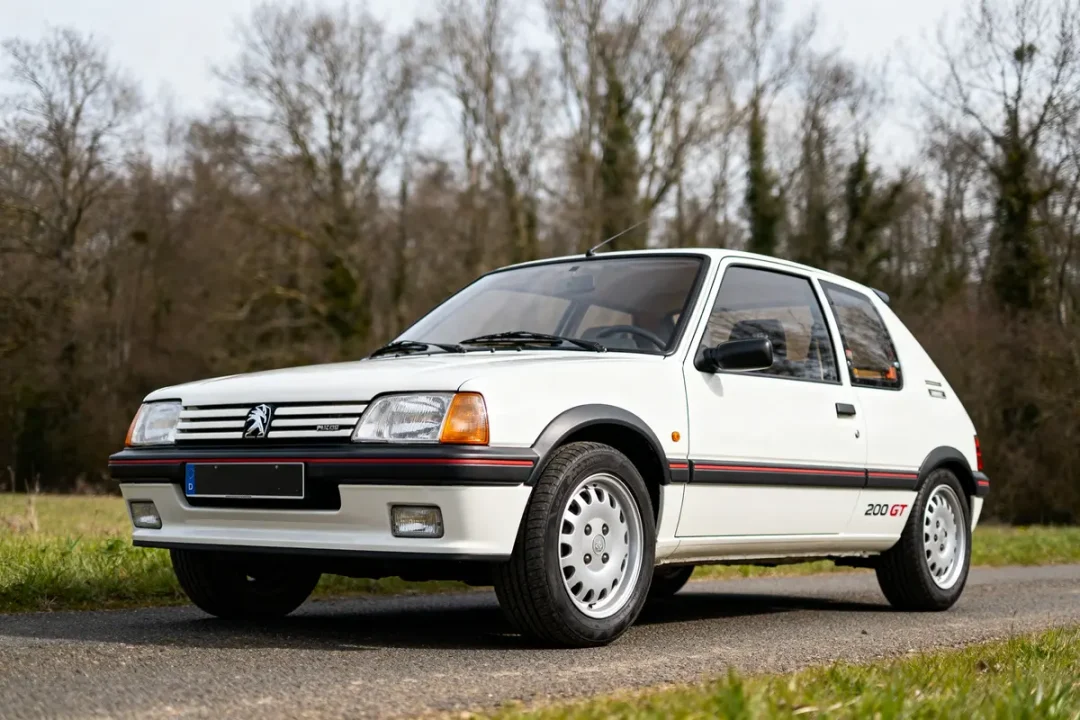 Peugeot 205 GTI automatic blanche garée sur une route devant un paysage boisé
