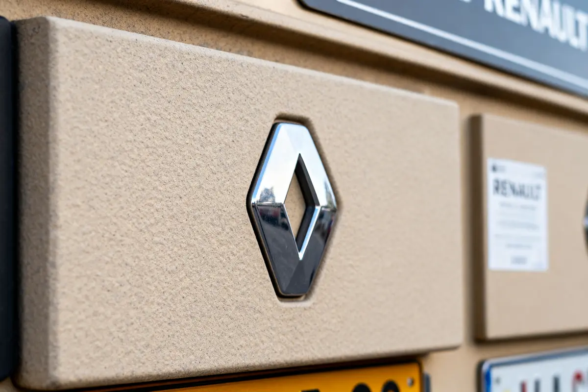 Renault logo argenté sur fond beige, avec des plaques et documents en arrière-plan