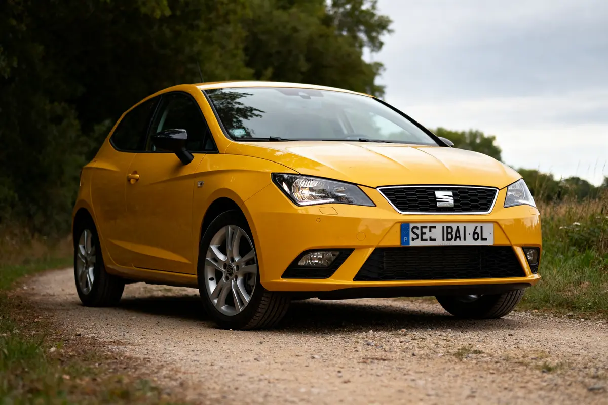 Voiture jaune SEAT Ibiza 6L garée sur chemin rural entouré de verdure.