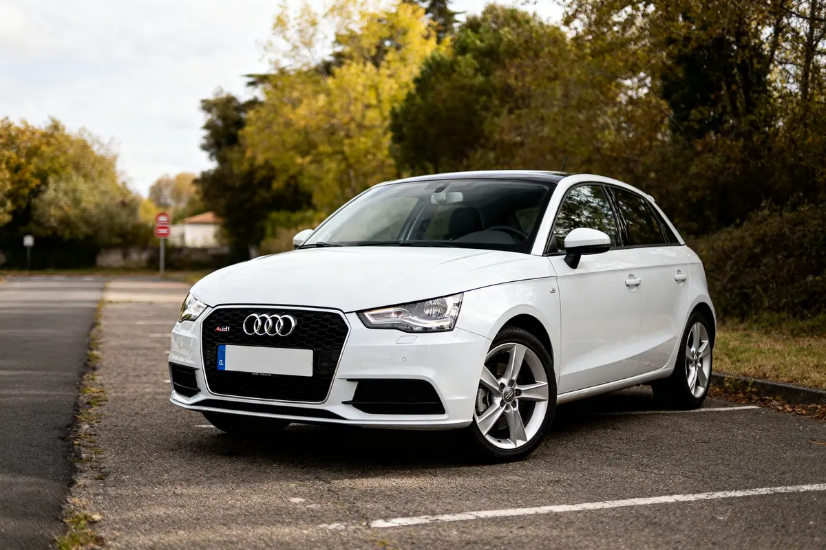 Automatic Audi A1 blanche garée sur parking, entourée de nature en arrière-plan