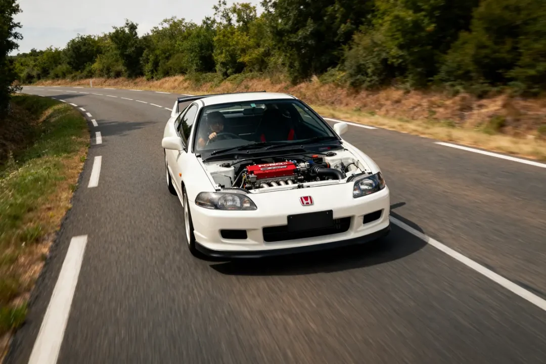 Voiture blanche sans capot roulant sur route campagnarde avec moteur exposé ctr Honda