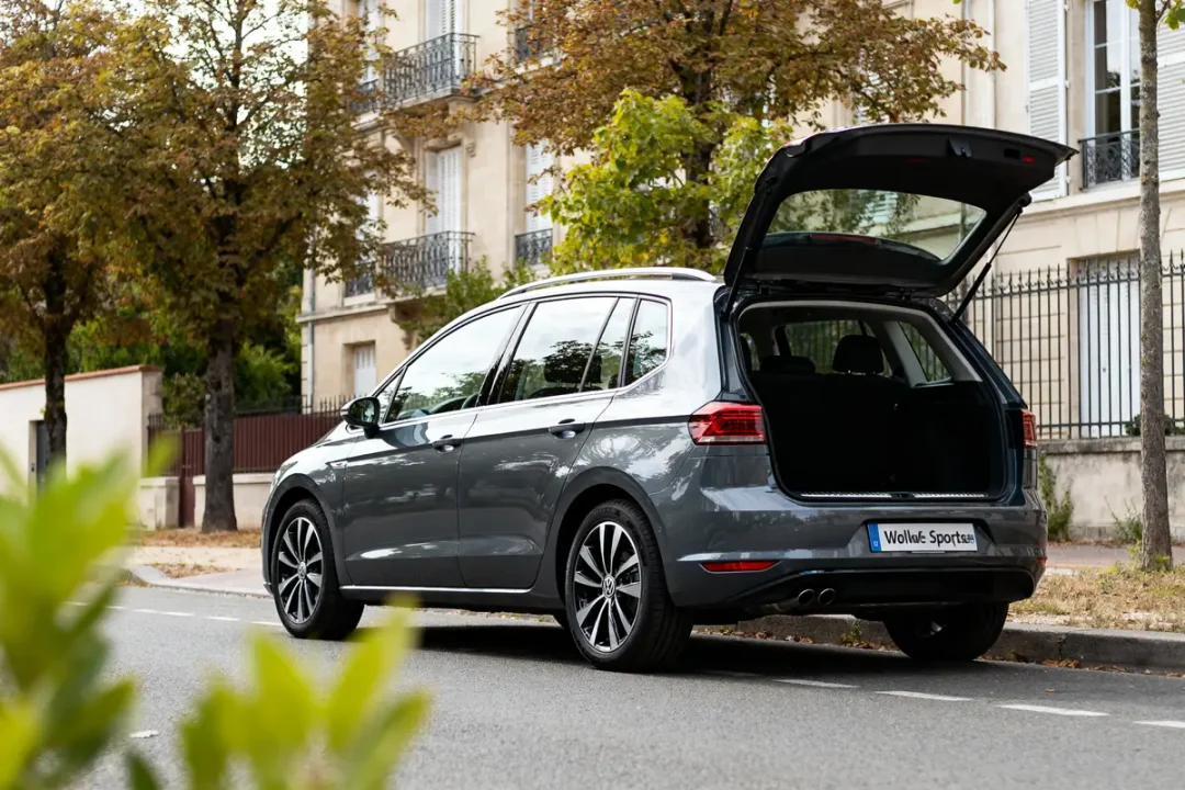 Vue arrière d'un Golf Sportsvan gris avec coffre ouvert devant bâtiments résidentiels