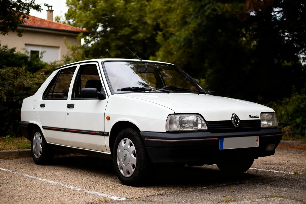 Voiture Renault 21 Sedan blanche garée sur un parking entouré de verdure