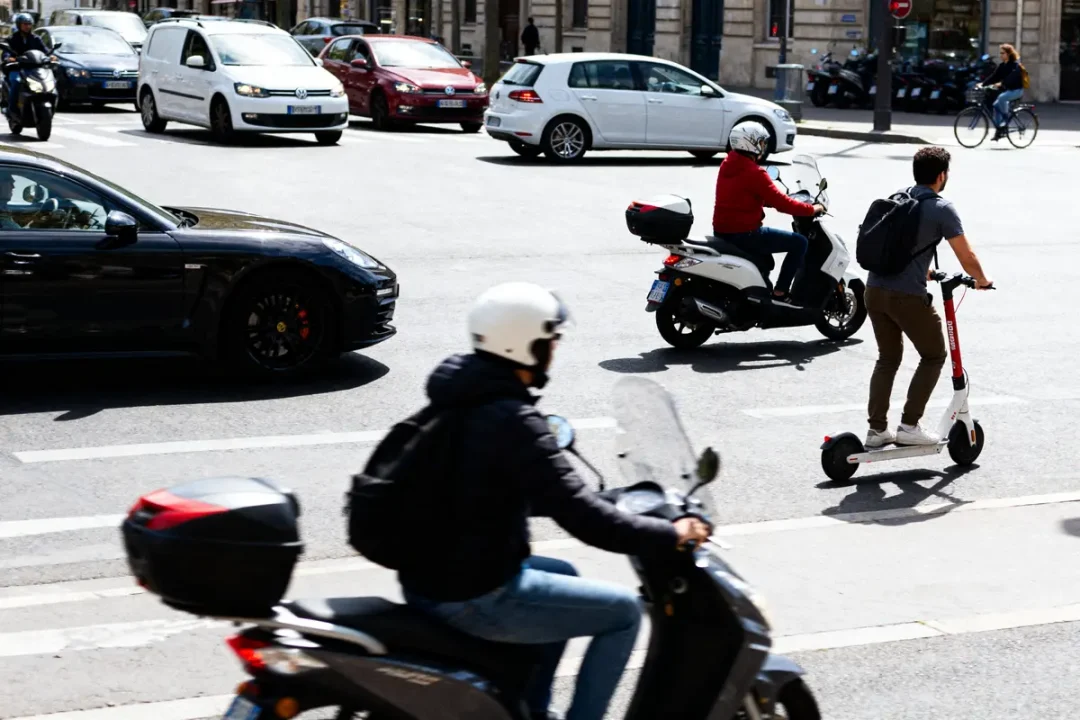 Homme en trottinette atoocycles et scooters en mouvement dans une rue animée.