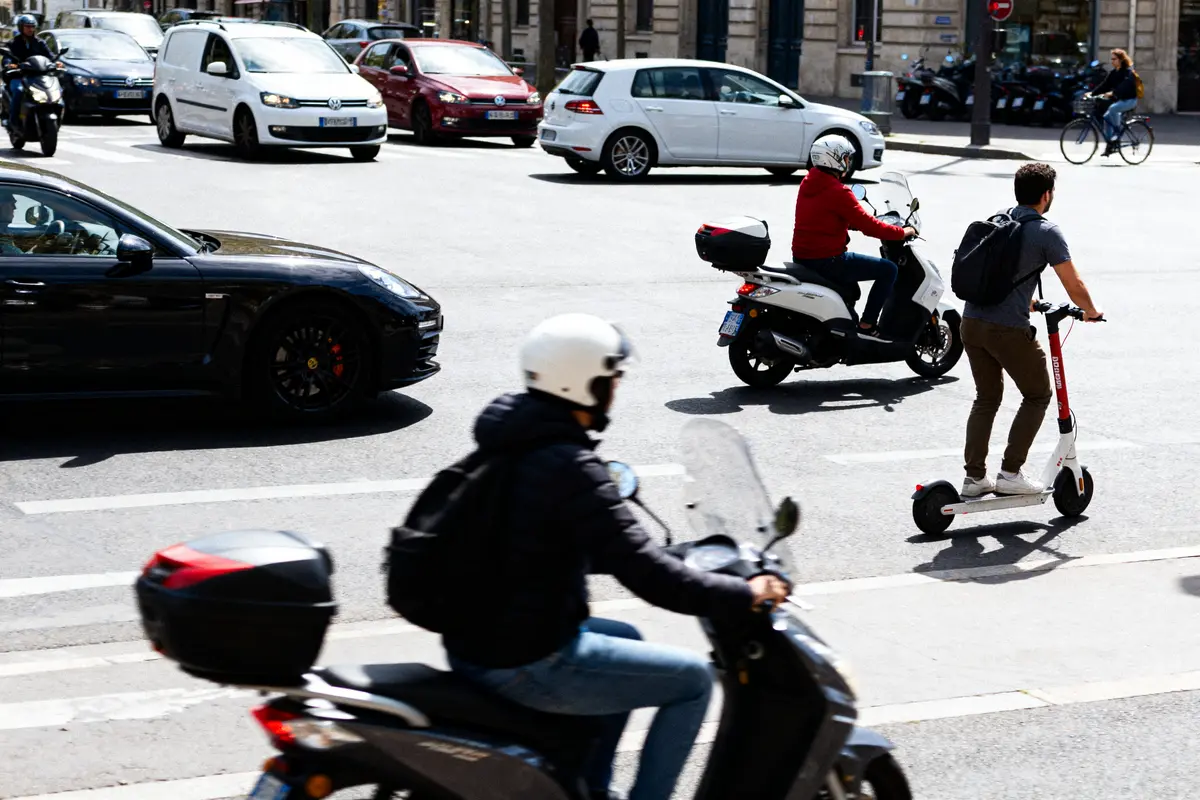 Homme en trottinette atoocycles et scooters en mouvement dans une rue animée.