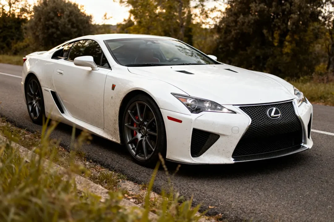 Supercar Lexus LFA blanche sur route bordée d'arbres et de végétation verte.