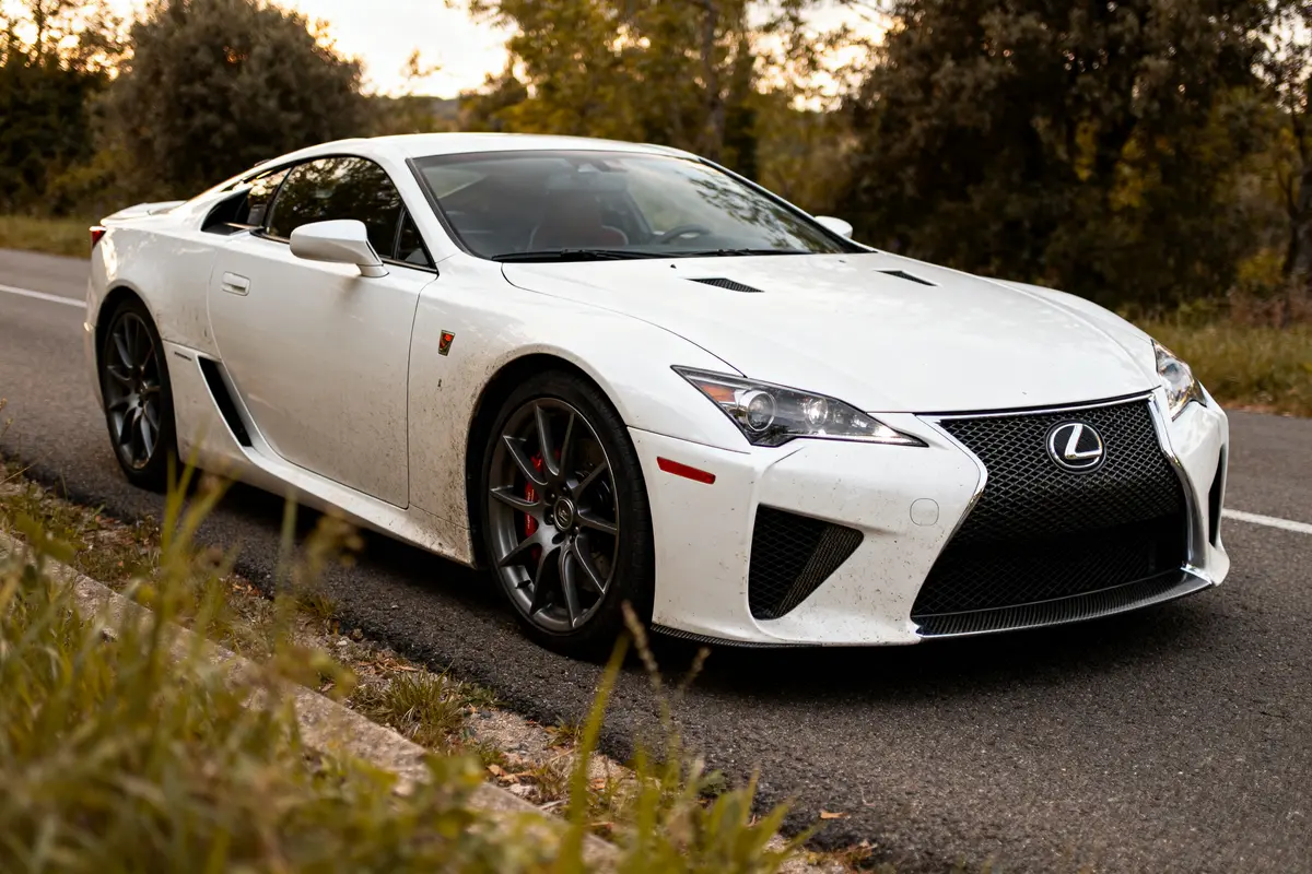 Supercar Lexus LFA blanche sur route bordée d'arbres et de végétation verte.